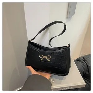 Detail showing the glossy crocodile texture and golden metal bow on the black shoulder bag