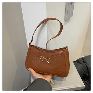 Macro view of brown crocodile texture and golden bow buckle on a shoulder bag