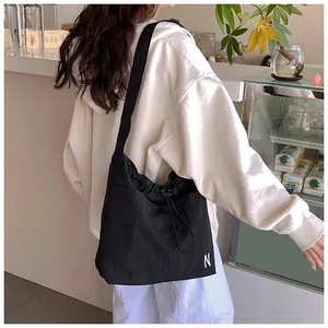 Detail of black drawstring crossbody bag with embroidered white N and wide fabric strap