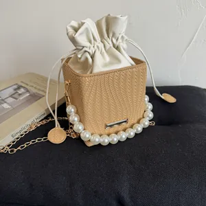 Detail of woven bucket bag featuring pearl handle, drawstring liner and gold chain