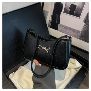 Detail of black faux crocodile leather bag with golden bow hardware in a premium gift box