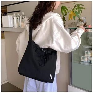 Detail of black drawstring crossbody bag featuring a white letter N print on a nylon surface