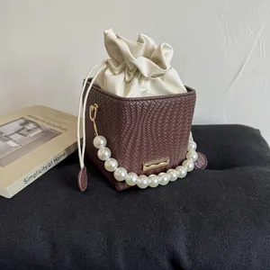 Detail of woven bucket bag with pearl handle and cream drawstring on black velvet