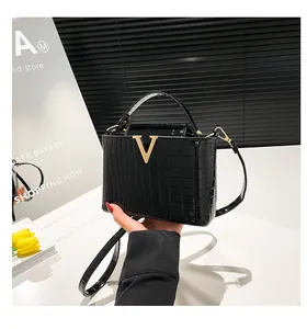 Detail of black crocodile-embossed patent leather bag with gold V logo and slim strap