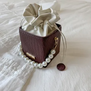 Detail of burgundy woven bucket bag with elegant large pearl handle and drawstring