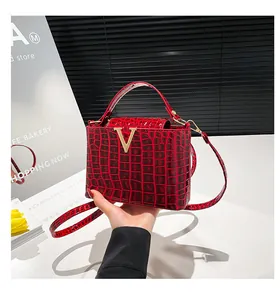 Detailed close-up of a red crocodile-textured handbag with a gold V-shaped metal buckle