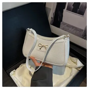 Detailed view of white crocodile texture shoulder bag with gold bow clasp in luxury gift box
