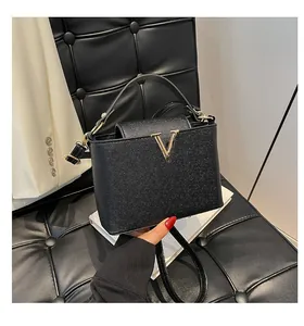 Détail du sac à main en cuir grainé noir avec logo métallique en V doré sur le devant du sac