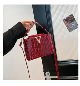 Detail of red crocodile pattern handbag with gold V-buckle and glossy leather finish