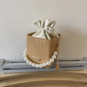 Chic woven bucket bag with pearl handle and cream drawstring pouch on a display stand