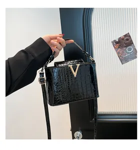 Close-up of black crocodile pattern leather handbag with gold V-shaped metal buckle detail