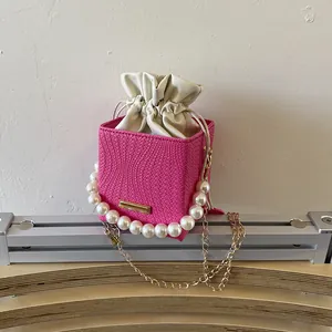 Pink woven bucket bag with pearl handle and gold chain strap for elegant women