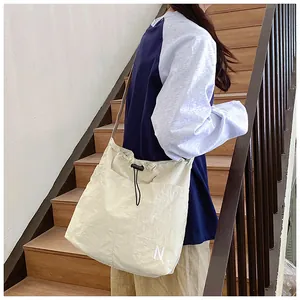 Close-up of drawstring closure and white 'N' embroidery on a beige nylon shoulder bag