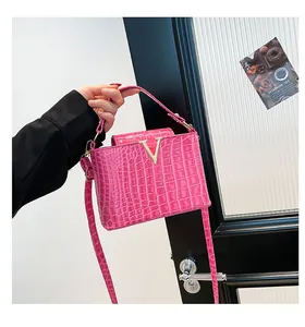 Detailed close-up of pink crocodile-embossed leather handbag with gold V-shaped logo and strap