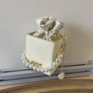 Chic cream woven bucket bag with elegant pearl top handle and gold metal accents