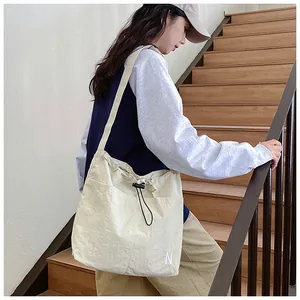 Detail of cream drawstring crossbody bag featuring N embroidery and nylon texture