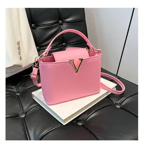 Détail macro du sac en cuir texturé rose avec logo métallique en forme de V doré