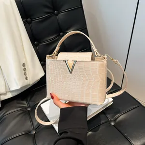Chic cream crocodile pattern tote bag with silver V buckle on a luxury sofa setting