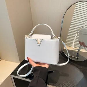 Sac à main en cuir blanc avec boucle en V dorée et poignée supérieure sur un bureau