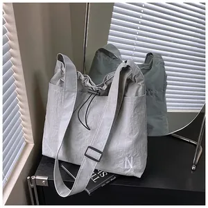 Detail of light grey nylon tote bag showing drawstring closure and white N embroidery