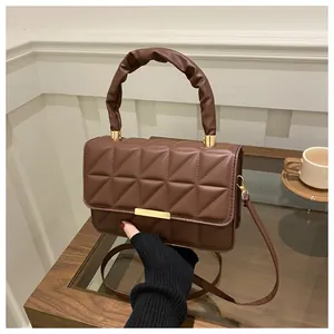 Detailed view of brown quilted leather bag with ruched handle and gold clasp on wood table
