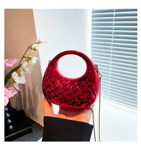 Detail of red metallic quilted clutch bag with golden chain strap held in hand