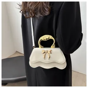 Detail view of cream white bow crossbody bag with golden handle and wavy flap design