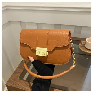 Detail of caramel crocodile pattern handbag with gold metal lock and chain strap