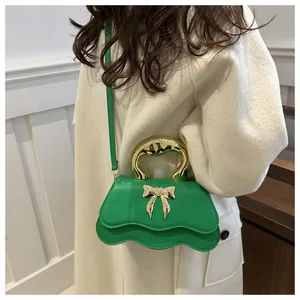 Emerald green crossbody bag with golden bow hardware and wavy edge detail on model