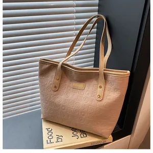 Close-up of beige tote bag featuring embossed letters and a golden metal logo plate