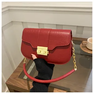 Detail of red crocodile texture handbag with golden buckle and chain strap on hand
