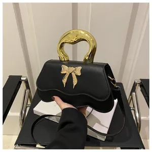 Detailed view of black matte handbag featuring wave-edge flap and golden bow metallic clasp