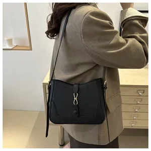 Detail of a black leather crossbody bag with a gold metal clasp shown on a model