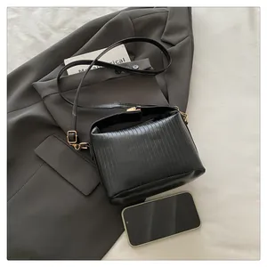 Detail of black pleated handbag with gold hardware and long shoulder strap