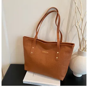 Detailed macro shot of brown leather tote featuring embossed letters and a gold logo plate