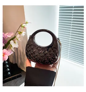Detail of black glossy handbag featuring diamond lattice texture and gold chain strap
