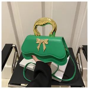 Detail of green crossbody bag with wavy bottom and gold bow handle accessory