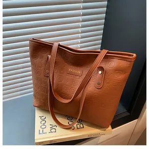 Close-up of brown faux leather tote bag with embossed letters and gold metal logo