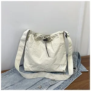 Detail of cream nylon crossbody bag featuring drawstring closure and functional front pockets