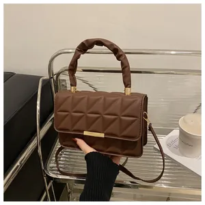 Detail of dark brown quilted crossbody bag with scrunchie handle and gold metal clasp