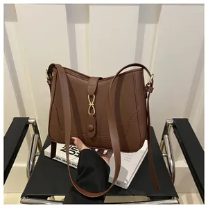 Detail of dark brown leather underarm bag with gold infinity buckle on a book