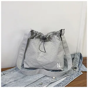 Close-up of light grey nylon crossbody bag with drawstring closure and white letter N