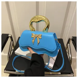 Close-up of bright blue crossbody bag with gold bow lock and wavy flap design