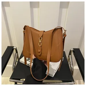 Close-up of brown faux leather shoulder bag with decorative golden knot buckle detail