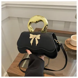 Detail of black crossbody bag with gold bow accent and unique curved bottom design