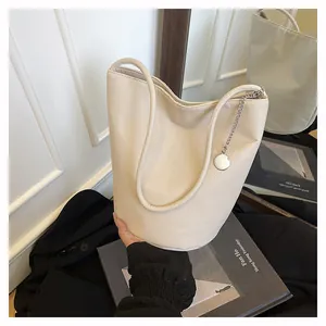 Detail of cream white leather bucket bag with silver chain charm against a lifestyle backdrop