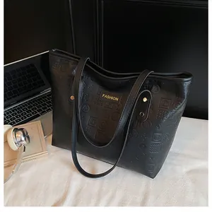 Detail of black tote bag with embossed letters, golden fashion plaque, and metal rivets
