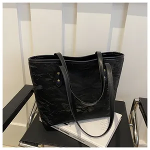 Detail of black tote bag featuring unique wrinkled texture and golden rivet reinforcement