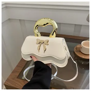 Detailed close-up of cream PU leather handbag featuring gold bow hardware and unique metal handle
