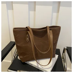 Detail view of the vintage pleated leather texture and metal rivets on a brown tote bag